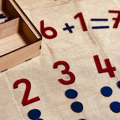 Jogo educativo com números vermelhos e fichas azuis em tecido bege e caixa de madeira clara