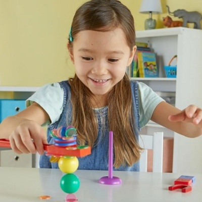 Menina brincando com brinquedo de empilhar de madeira colorido numa mesa branca