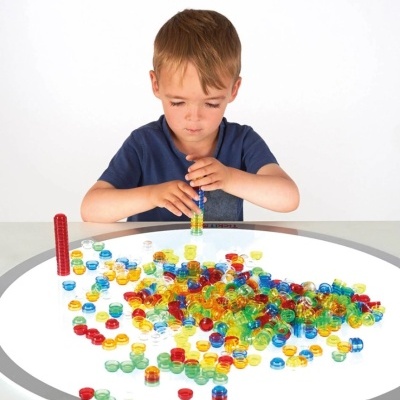 Criança em mesa iluminada a brincar com peças plásticas coloridas