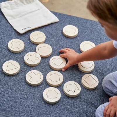 Peças de madeira claras com formas geométricas gravadas e um saco de tecido branco com texto 'Tickit'