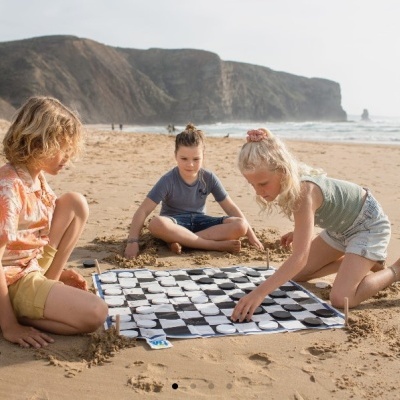 Crianças jogando damas em tabuleiro quadriculado na praia