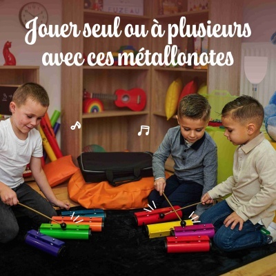 Três crianças a tocar xilofones coloridos de metal no chão de um quarto infantil