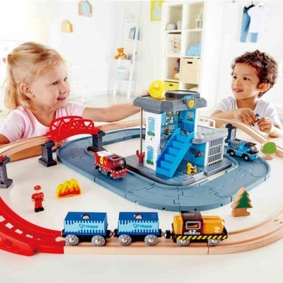 Brinquedo de comboio de madeira com figuras e estruturas azuis, vermelhas e castanhas numa mesa com crianças a brincar