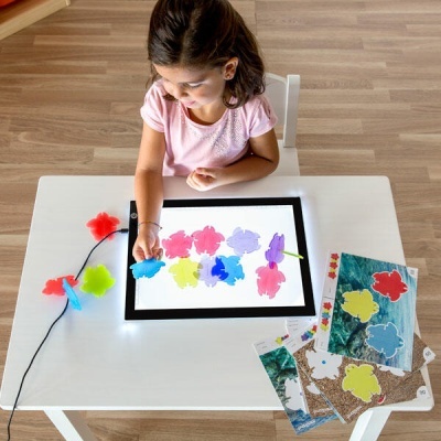 Criança a brincar com peças translúcidas coloridas sobre superfície de mesa luminosa branca.