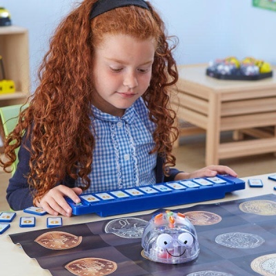 Menina a usar robô educativo abelha sobre mesa com tapete de moedas e peças azuis