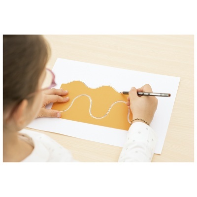 Criança a desenhar numa folha branca usando uma peça de papel castanha com traço ondulado branco.