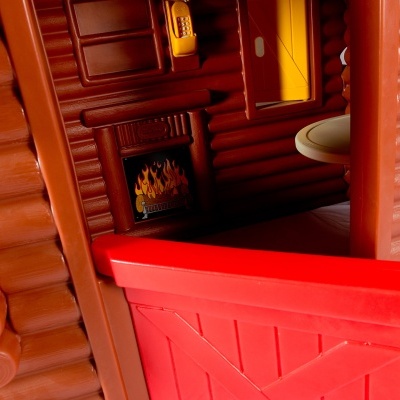 Interior de casinha de brinquedo com parede castanha, lareira, telefone amarelo e porta vermelha