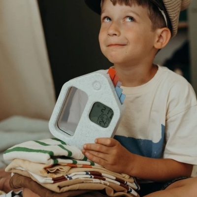 Menino com termómetro digital em forma de casa e roupas dobradas