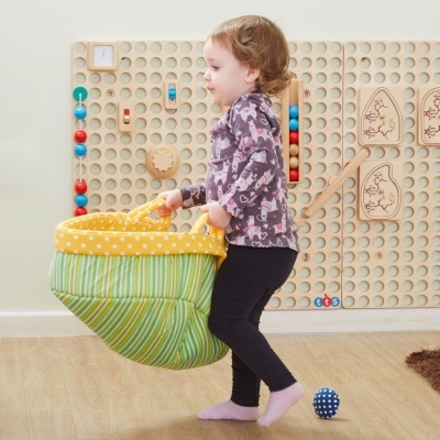 Criança a segurar saco de tecido com padrão listrado e bolinhas em ambiente com painel de madeira para brincadeiras