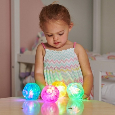 Menina pequena a olhar para bolas luminosas coloridas numa mesa de madeira clara num quarto de criança