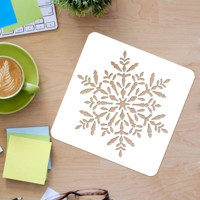 Stencil branco com padrão de floco de neve numa mesa de madeira com objetos de escritório