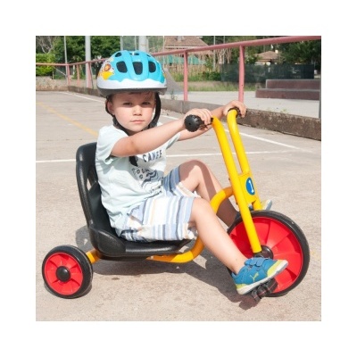 Criança em triciclo amarelo com roda vermelha e capacete azul num espaço exterior