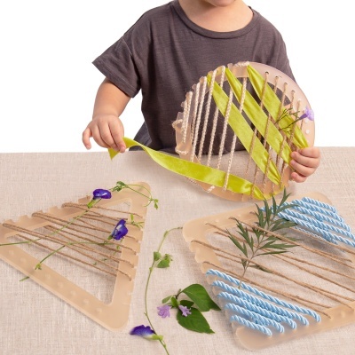 Criança a tecer fios coloridos em moldes triangulares com plantas e flores naturais