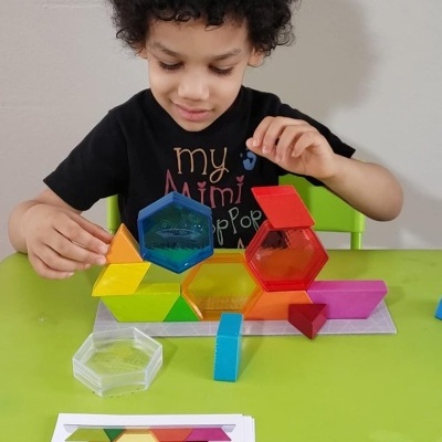 Criança a brincar com blocos de construção coloridos em plástico translúcido numa mesa verde.