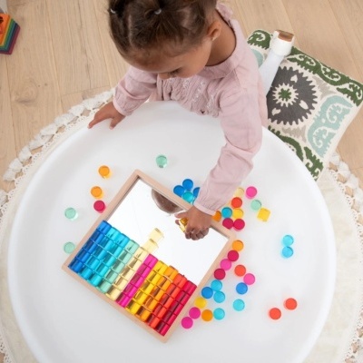 Criança a brincar com discos coloridos e espelho numa superfície redonda branca