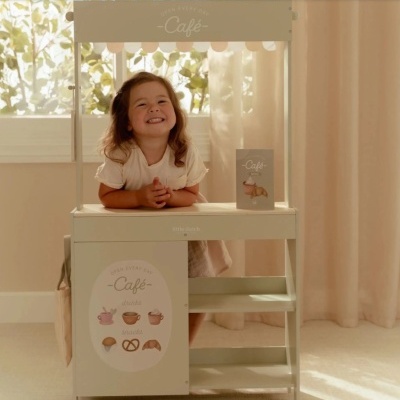 Menina sorridente numa banca de madeira com tema café em ambiente interior