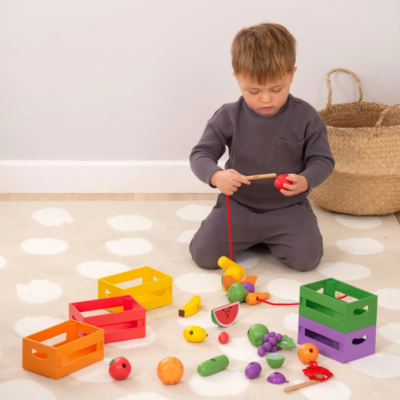 Criança brinca com brinquedos coloridos de madeira num tapete claro junto a um cesto de palha