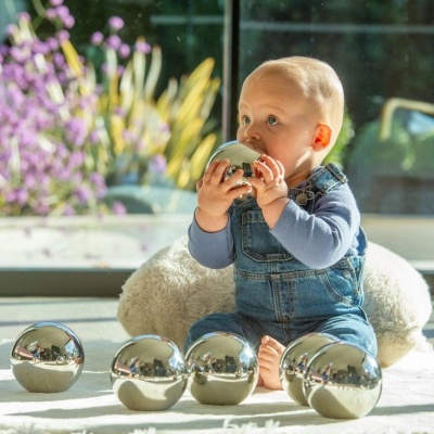 Bebé com macacão a brincar com bolas metálicas prateadas