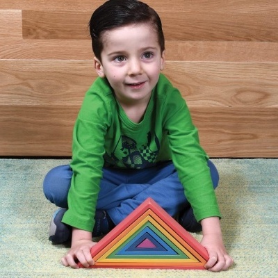 Menino com camiseta verde e calças azuis segurando brinquedo triangular colorido sentado no chão