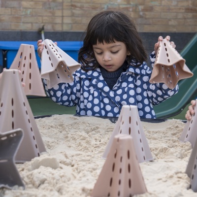 Criança a brincar com cones de plástico na areia