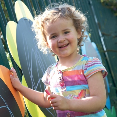 Camisola de riscas coloridas usada por criança junto a estrutura de brincar verde