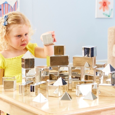 Menina a brincar com blocos metálicos prateados em mesa de madeira