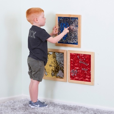 Três painéis de lantejoulas coloridas em molduras de madeira na parede com chão de tapete cinza