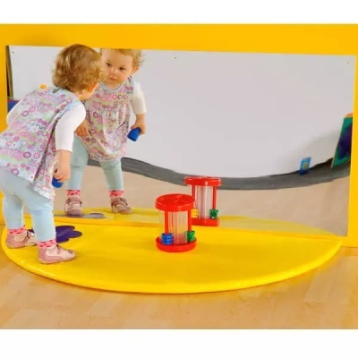 Espelho grande com moldura amarela e criança refletida junto com duas ampulhetas de plástico vermelho.