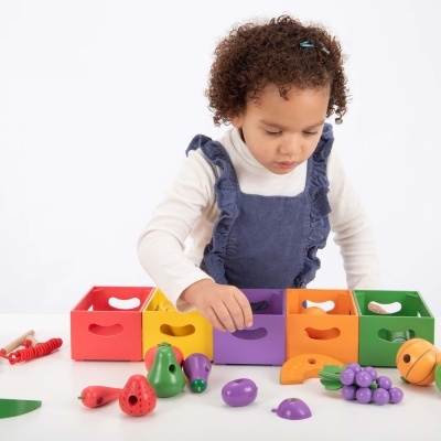 Criança a brincar com brinquedo educativo de madeira colorido com frutas e legumes.