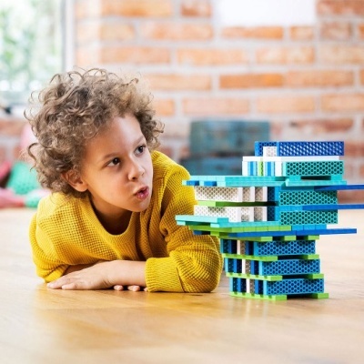 Criança com camisola amarela de malha ao lado de torre de blocos coloridos