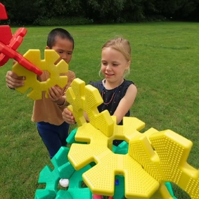 Crianças com peças grandes de plástico tipo engrenagem num relvado