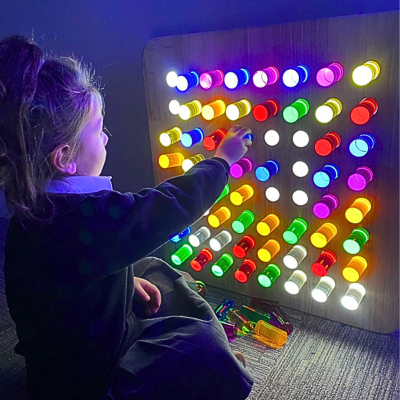 Menina a brincar com painel de luzes coloridas em base de madeira