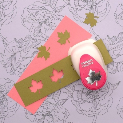 Cortador de papel vermelho e branco para recortes em forma de folha, em fundo decorado