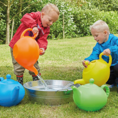 Crianças a usar regadores coloridos em relva ao lado de uma bacia metálica