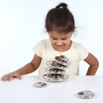 Menina sorrindo a olhar discos metálicos prateados empilhados numa mesa branca