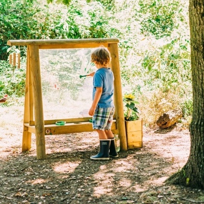 Mesa de atividades infantil ao ar livre com estrutura de madeira clara e painel transparente para desenho