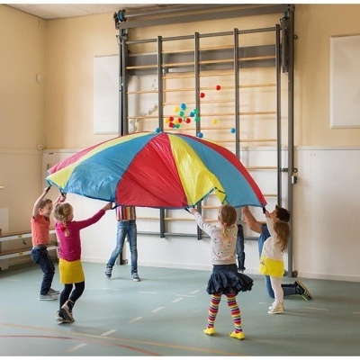 Crianças a brincar com um paraquedas colorido em ginásio escolar
