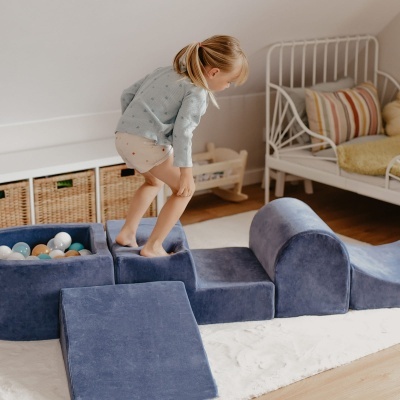 Brinquedo modular azul de tecido aveludado com piscina de bolas coloridas e criança a brincar