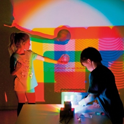 Crianças brincam com blocos coloridos e projetam luz na parede
