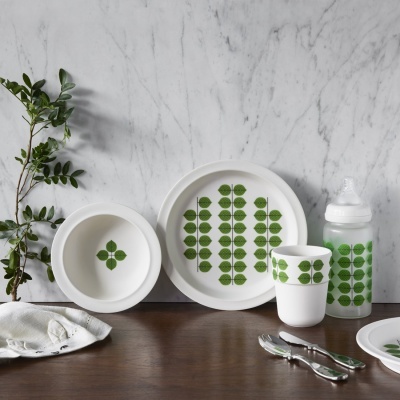 Conjunto de louça branca com padrão de folhas verdes para crianças em cima de mesa de madeira