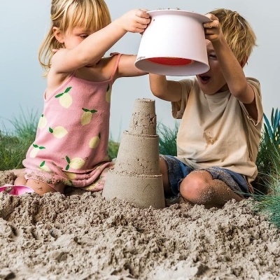 Crianças a brincar na areia com balde e torre de areia