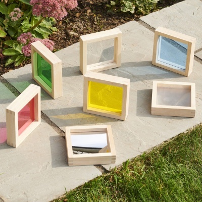 Brinquedos de madeira quadrados com superfícies coloridas e espelhadas sobre pavimento exterior