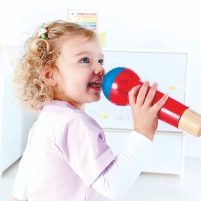 Criança segurando microfone de madeira colorido em ambiente claro