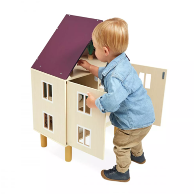 Criança a brincar com casa de bonecas em madeira com telhado roxo