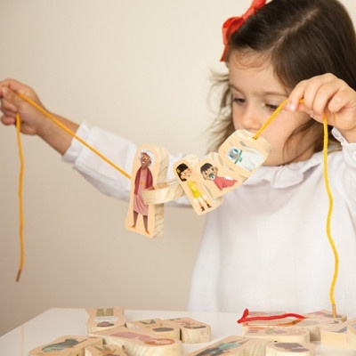 Criança brinca com peças de madeira ilustradas ligadas por um cordão amarelo