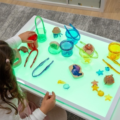 Mesa de luz com objetos de plástico colorido e criança a brincar