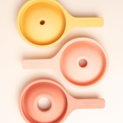 Três funis de silicone amarelo e rosa, cada um com câmara circular e alça com texto INSPIRE