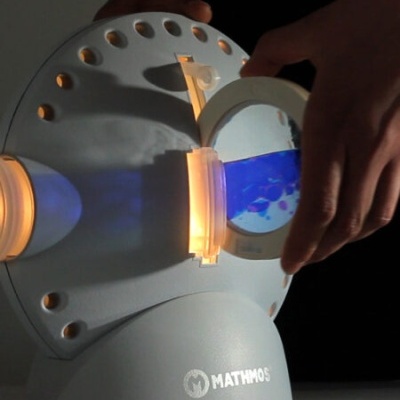 Aparelho circular branco iluminado com marca MATHMOS e líquido azul ajustado por mãos.