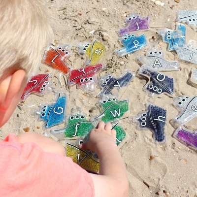 Jogo educativo de letras coloridas em plástico translúcido numa praia com criança
