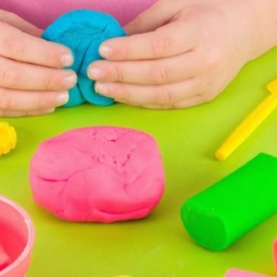 Massas de modelar coloridas e mãos infantis a manipulá-las numa superfície verde